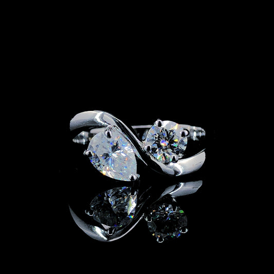 A sterling silver ring featuring a pear-cut and a round-cut moissanite, displayed against a black background.